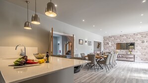 A modern kitchen with a central island, pendant lighting, and a dining area with a stone wall backdrop. - Appletrees (8), Burnham Market, Norfolk (Burnham Market)