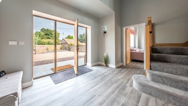 A spacious room with a large sliding glass door leading to an outdoor area, a staircase, and a small seating area with a bench and a plant. - Appletrees (8), Burnham Market, Norfolk (Burnham Market)