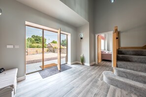 A spacious room with a large sliding glass door leading to an outdoor area, a staircase, and a small seating area with a bench and a plant. - Appletrees (8), Burnham Market, Norfolk (Burnham Market)