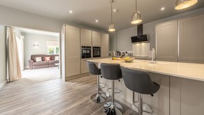 A modern kitchen with a central island, bar stools, pendant lighting, and a view into the adjacent living area. - Appletrees (8), Burnham Market, Norfolk (Burnham Market)
