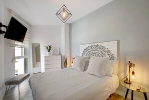 Ein Schlafzimmer mit Bett, Schreibtisch, Fernseher, Wanddekoration und einer Pendelleuchte.