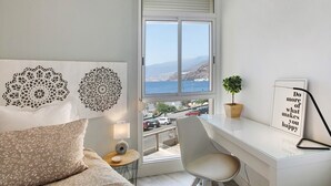 Ein Schlafzimmer mit großem Fenster, einem Bett, einem Schreibtisch, einem Stuhl und Wanddekoration.