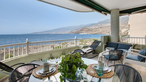 Ein Balkon mit Tisch für zwei Personen, mit Blick auf einen Strand und das Meer.
