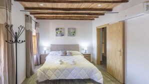 Ein Schlafzimmer mit Holzbalkendecke, einem Bett mit weißer Bettdecke, Nachttischen mit Lampen und einem Holzschrank.