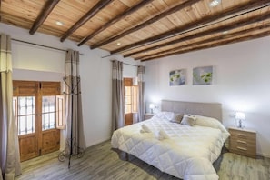 Ein Schlafzimmer mit Holzboden, einem Bett mit Steppdecke, einem Nachttisch und einer Tür mit Vorhängen.