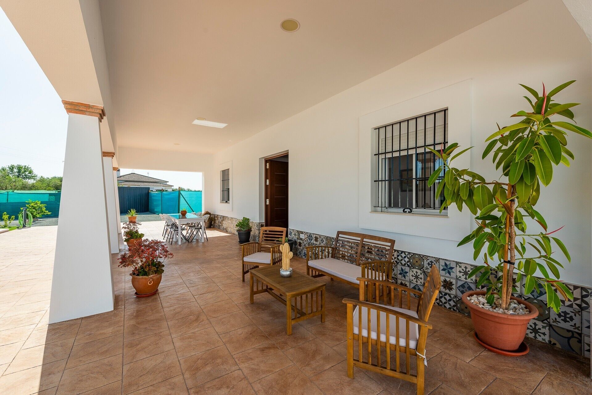A covered patio with a dining set, potted plants, and a view of the outside.
