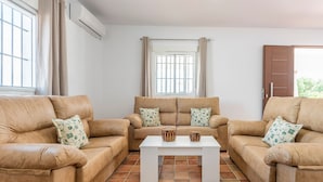 A living room with two beige sofas, a white coffee table, and a window with curtains. - Villa "Casa Brisa del Valle" with Private Pool, Covered Terrace & Wi-Fi (Sevilla)