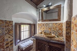 A bathroom with patterned tiles, a wooden vanity, a sink with a decorative basin, and a window with a towel rack.