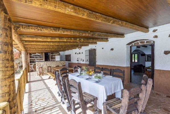 A rustic dining area with stone walls, wooden beams, and a white table set for a meal.