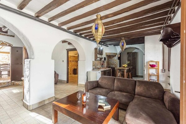 Una sala de estar con sofá, mesa de centro y chimenea. Hay dos lámparas colgantes y una estantería.