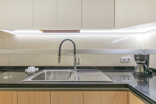 A kitchen with a stainless steel sink, a modern faucet, a coffee maker, and wooden cabinets.