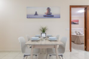 Ein Essbereich mit einem für sechs Personen gedeckten Tisch, einem gerahmten Bild an der Wand und Blick in ein Schlafzimmer durch eine offene Tür.