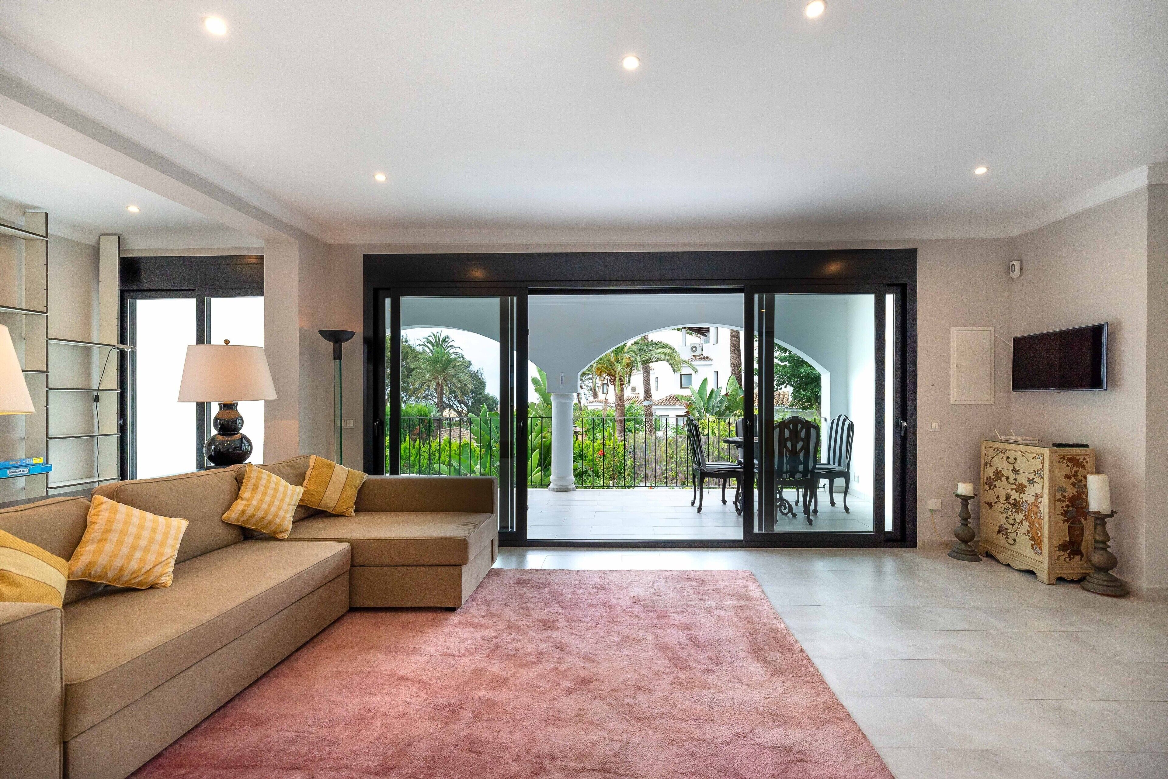 Un salon avec un canapé, un tapis, un téléviseur et une vue sur l’extérieur.