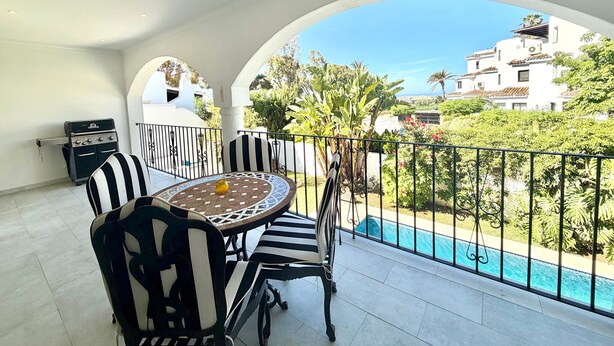 Un balcon avec une table et des chaises, un barbecue et une vue sur la piscine.