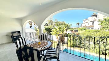 Un balcon avec une table et des chaises, un barbecue et une vue sur la piscine.