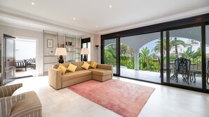 Un salon moderne avec un canapé d’angle, une table basse et une grande porte-fenêtre coulissante donnant sur un balcon aménagé avec du mobilier d’extérieur.