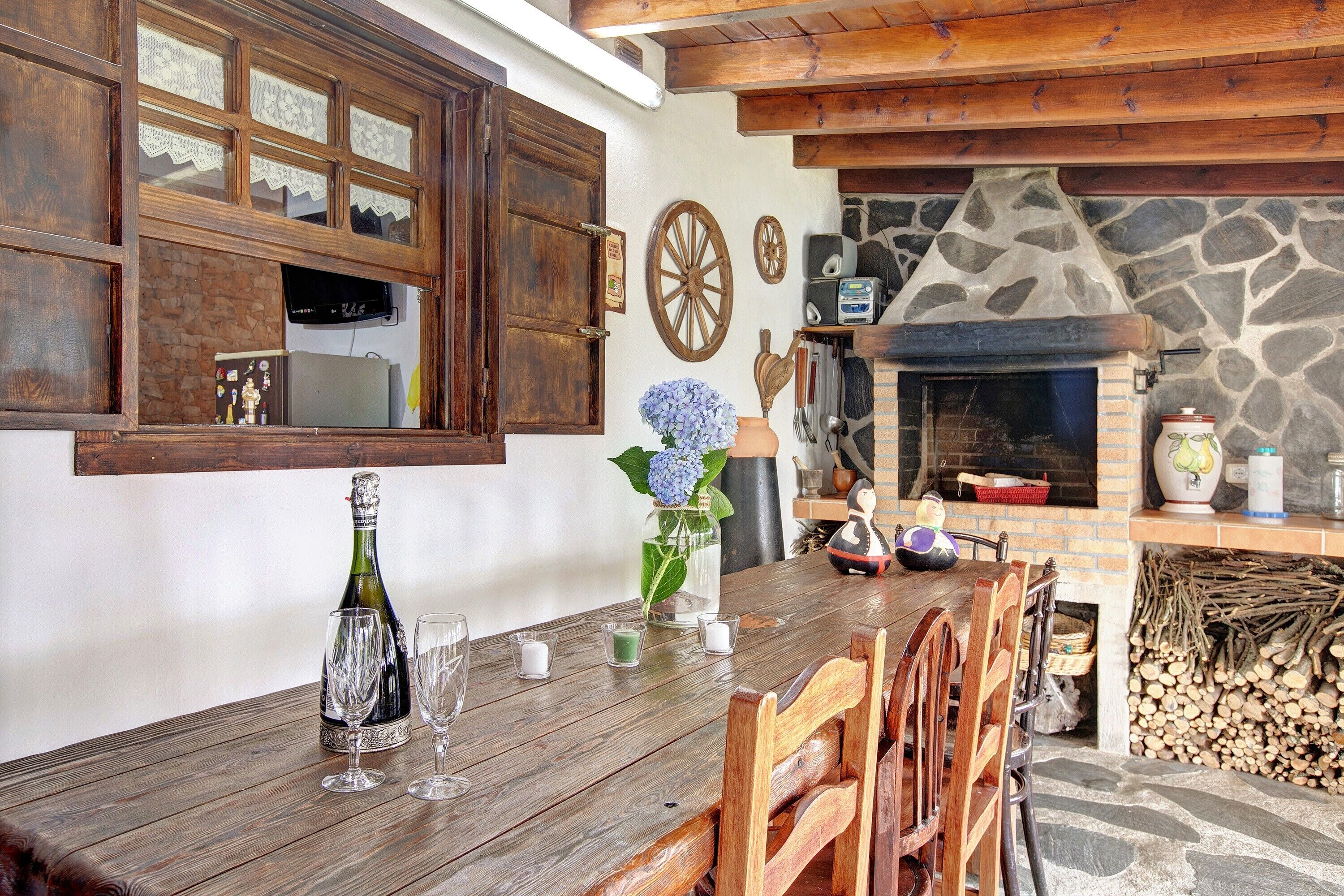 Un comedor rústico con una mesa de madera, sillas, una chimenea y una pared de piedra.