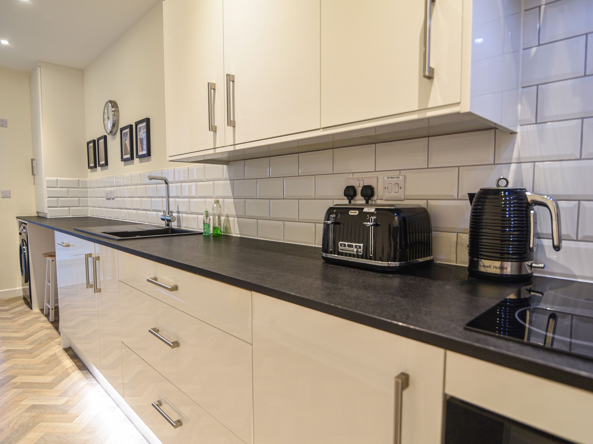 A modern kitchen with white cabinets, a black countertop, a toaster, and a kettle.