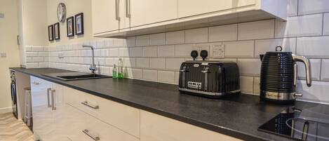 A modern kitchen with white cabinets, a black countertop, a toaster, and a kettle.