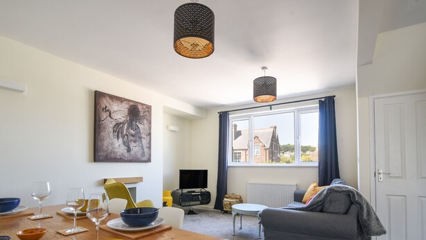 A modern living room with a dining area, a television, and a large window with curtains. - Bahari (Lyme Regis)