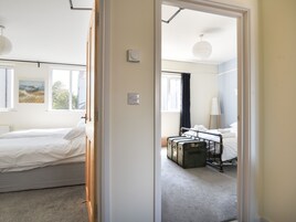 Una habitación de hotel con cama, radiador, ventana con un cuadro y maleta en el suelo.