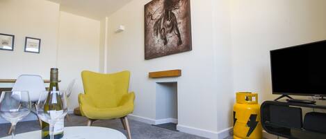 Un salon avec une table ronde, deux chaises, une cheminée, un tableau, un téléviseur et une bouteille de gaz jaune.