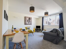 Una sala moderna con comedor, un sofá gris y un televisor.