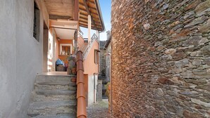 A narrow stone-paved alleyway flanked by buildings with a wooden staircase and a stone wall.