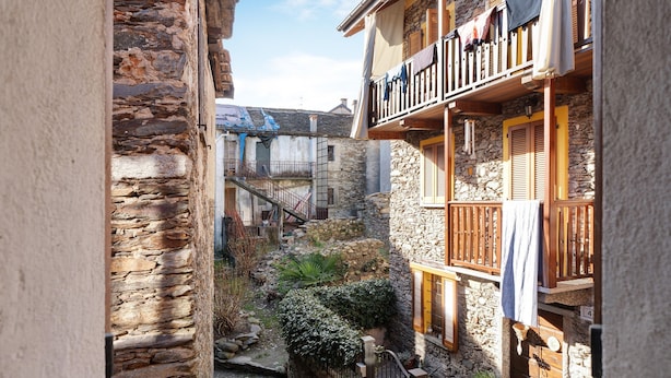 A narrow alleyway with stone buildings, wooden balconies, and a small garden area.