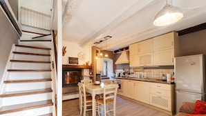 A kitchen with wooden cabinets, a dining table with chairs, a refrigerator, and a staircase.