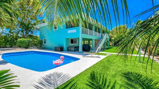 A two-story house with a swimming pool, a pink flamingo float, and a well-maintained lawn. - Pozitively Bliss updated 3bed/2bath single family home near Sombrero Beach with private pool & dockage (Marathon)