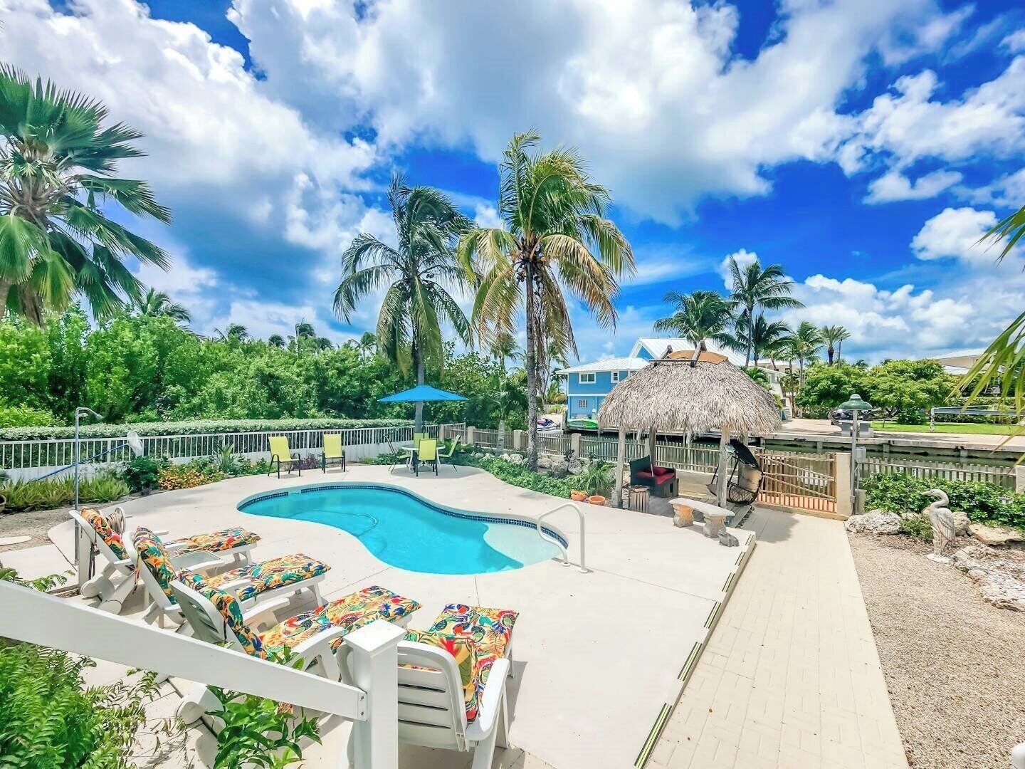 A pool area with lounge chairs, a thatched-roof structure, and palm trees.