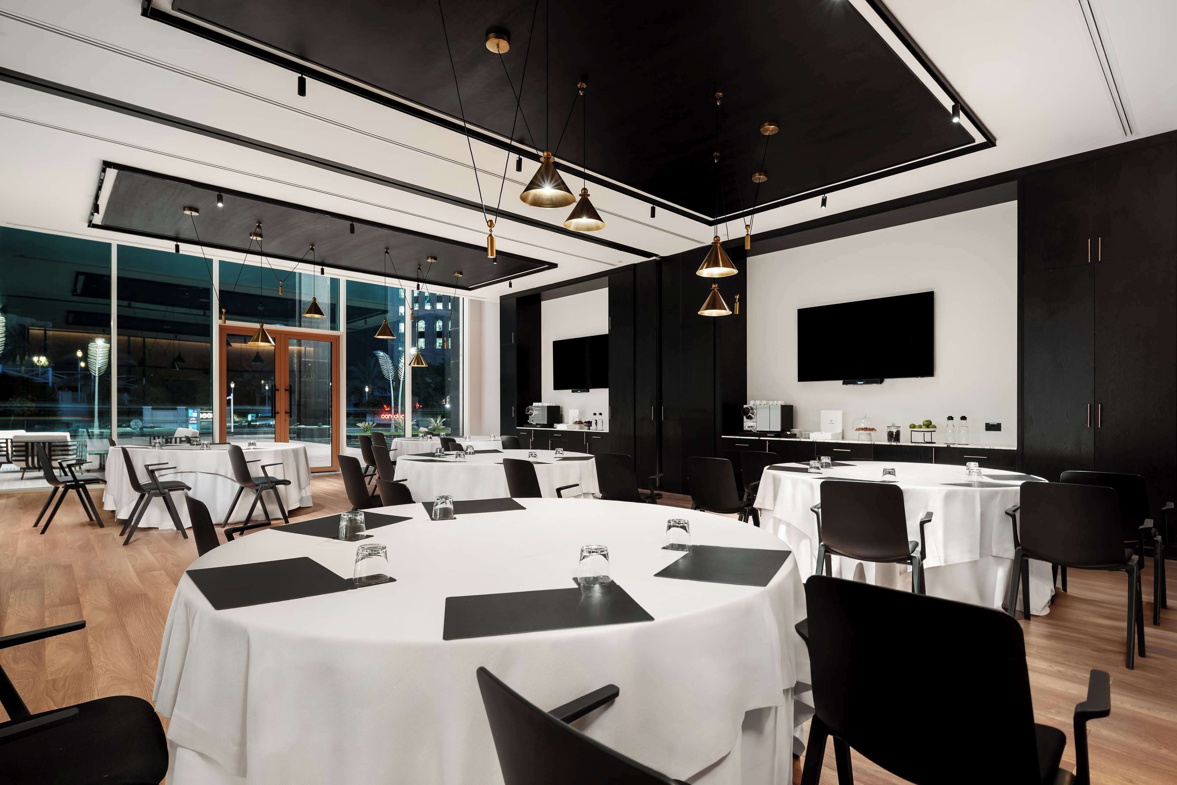 A modern conference room with round tables, black chairs, and a large TV screen.