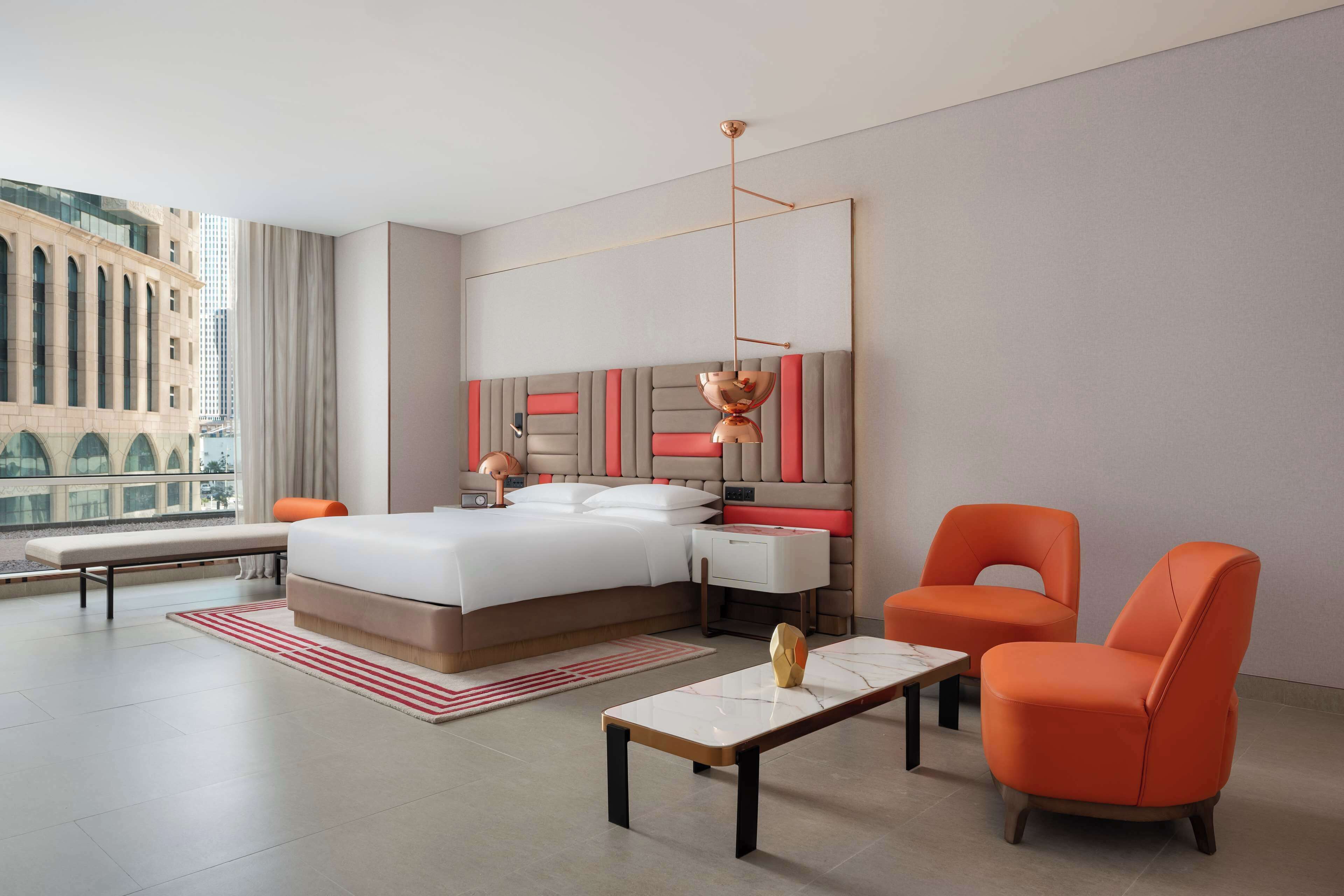 Habitación de hotel moderna con una cama grande, un escritorio, dos sillas y vistas a la ciudad.