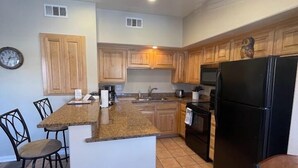 A kitchen with wooden cabinets, a black refrigerator, a sink, and a clock on the wall. - Kings Court by Mesquite Vacation Rentals with Community Pool and $510 in free daily activities (Mesquite)