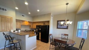 A modern kitchen with wooden cabinets, a black refrigerator, and a dining area with a round table and chairs. - Kings Court by Mesquite Vacation Rentals with Community Pool and $510 in free daily activities (Mesquite)