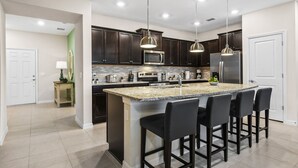 A modern kitchen with dark wood cabinets, a granite island with bar stools, stainless steel appliances, and pendant lighting. - PROMO Beautiful 5 BR Home,Private Pool,Resort - by Blue Sky Villas (Davenport)