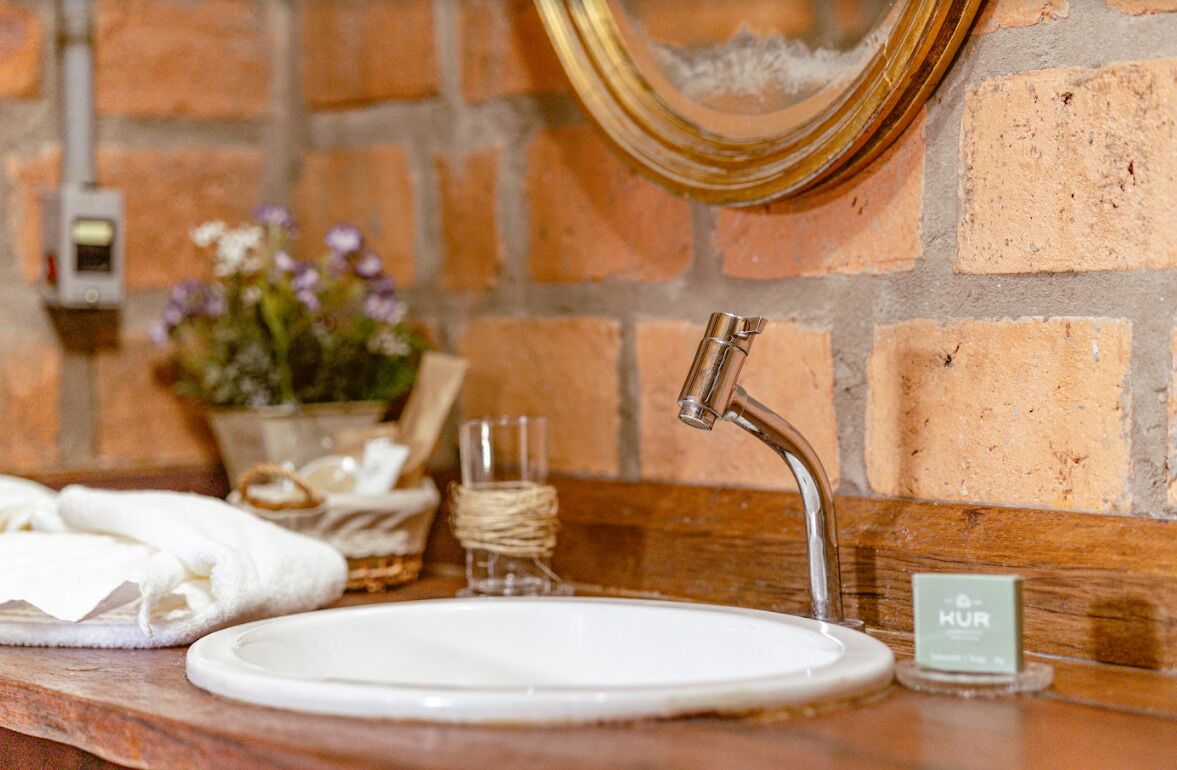 A bathroom with a white sink, a gold faucet, a mirror, and a brick wall.