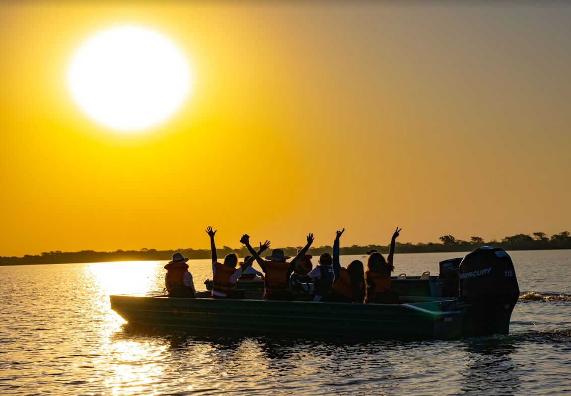 Un bote con pasajeros levantando las manos al atardecer.