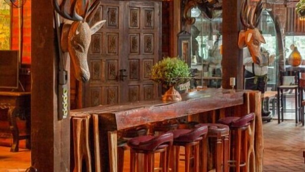 Un interior rústico con vigas de madera, una zona de bar con taburetes y adornos de asta de ciervo.