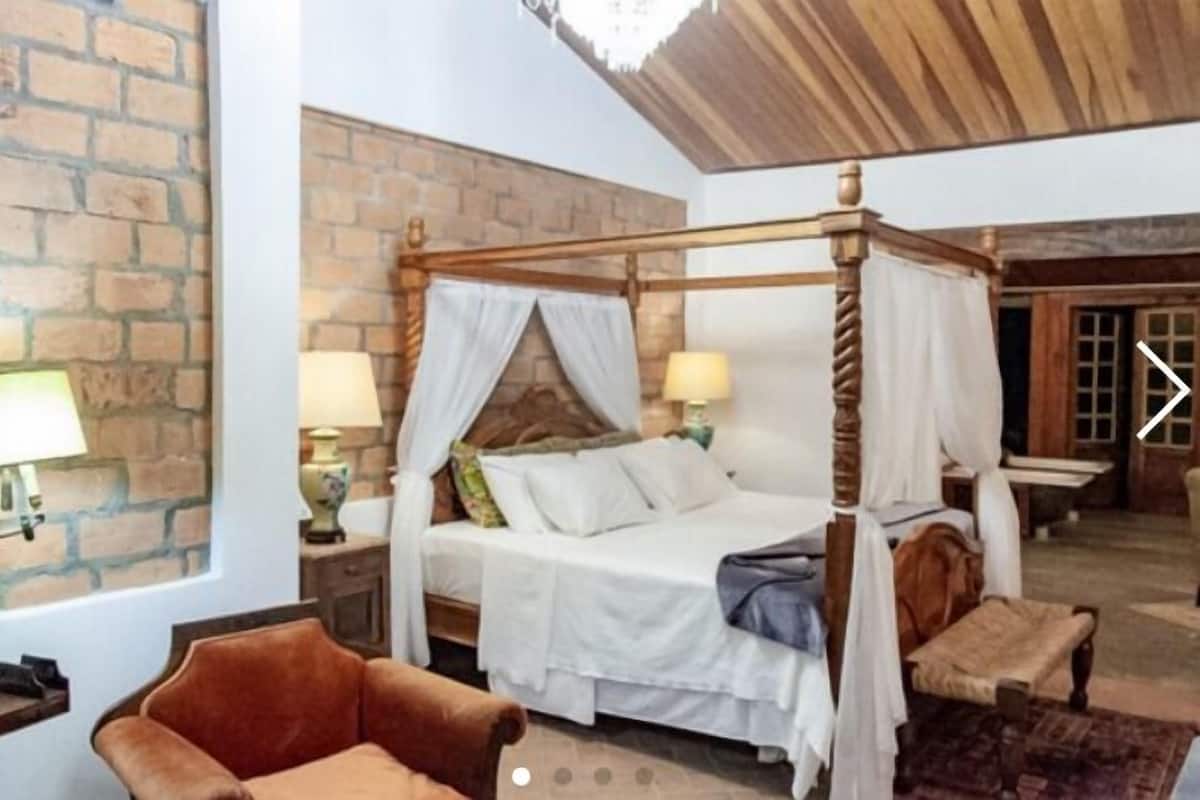 A room with a four-poster bed, a brick wall, and a wooden ceiling.
