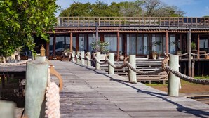 Un paseo marítimo de madera que conduce a un edificio tradicional con ventanas amplias y un nivel superior cubierto.