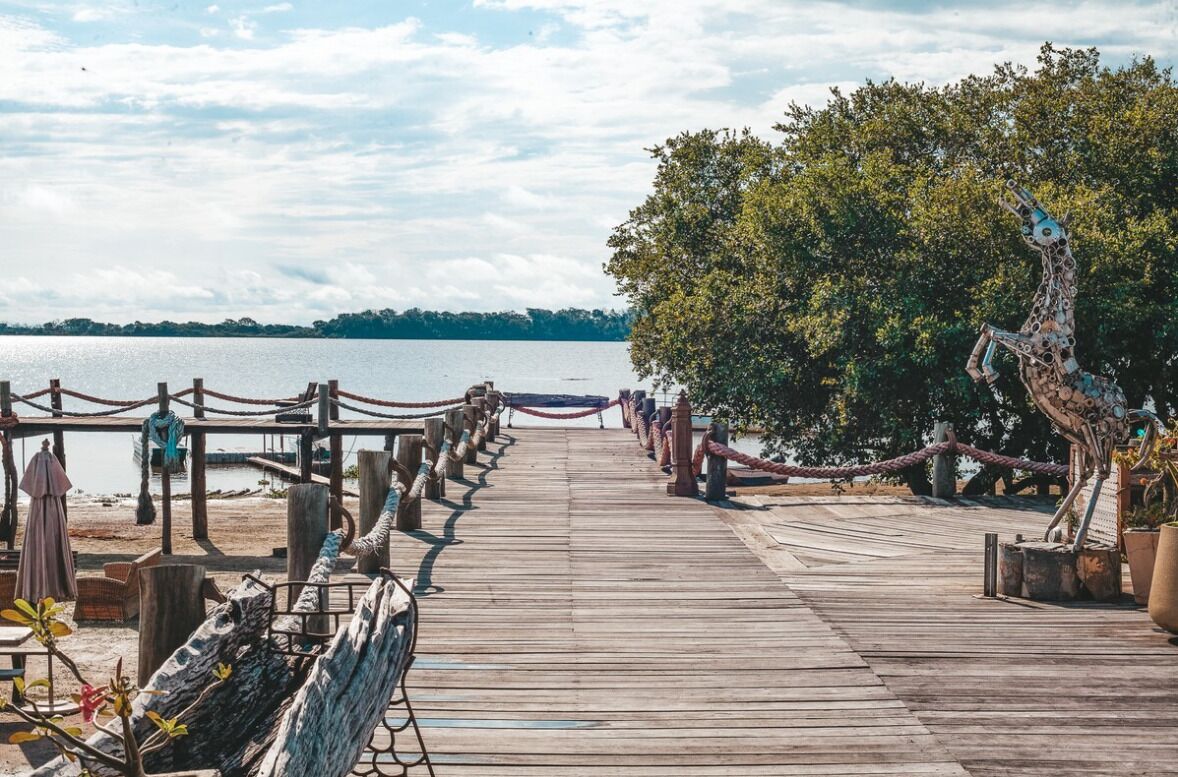 Un muelle de madera que lleva a una playa, con una escultura de jirafa a la derecha.