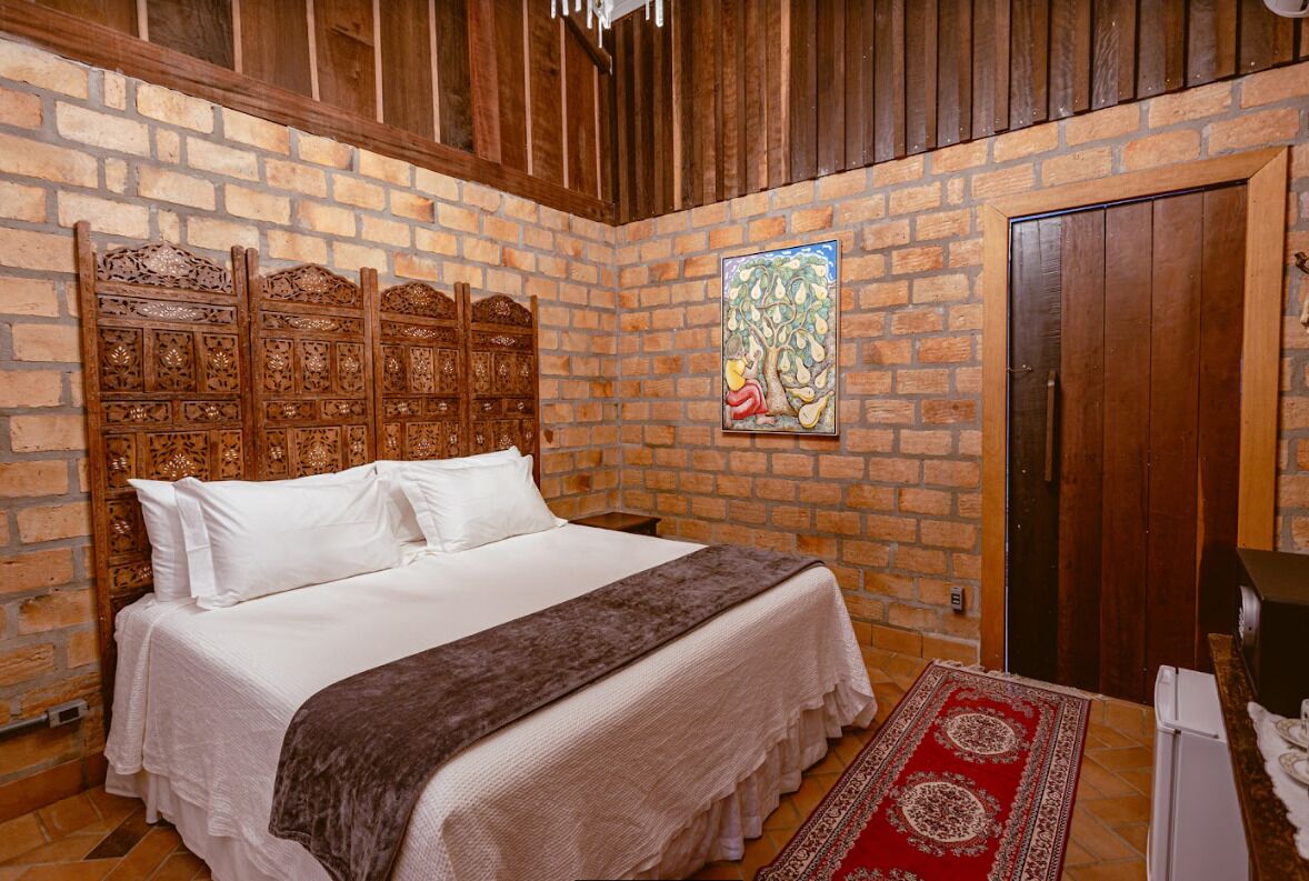 A bedroom with a brick wall, a wooden headboard, a bed with white bedding, a red and white patterned rug, and a door.