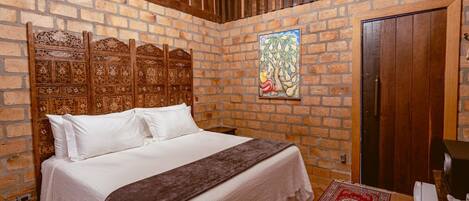 A bedroom with a brick wall, a wooden headboard, a bed with white bedding, a red and white patterned rug, and a door.