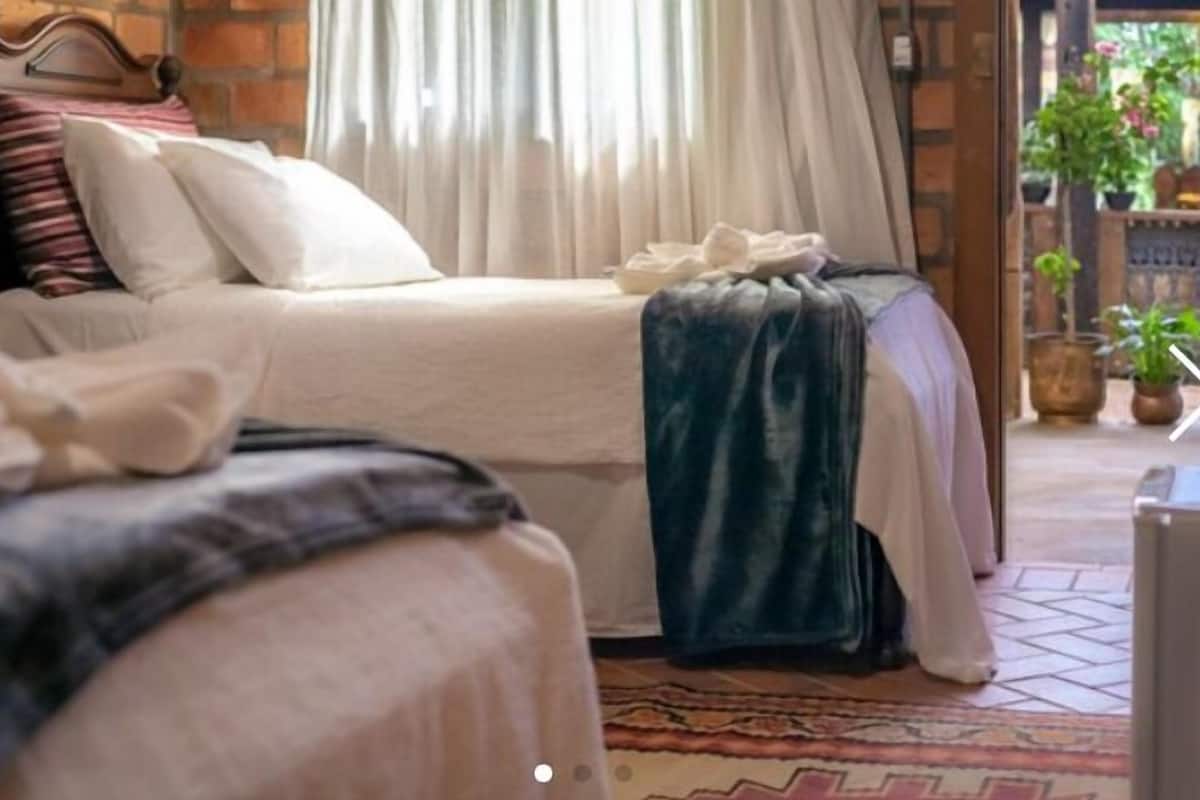 A bedroom with two beds, a wooden headboard, and a view of the outdoors through a window with curtains.