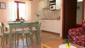 A compact kitchen with white cabinets, a microwave, and a sink. There is a dining table with chairs and a small potted plant on a table runner. - Vacation home Milva by Interhome (Pula/Rakalj)