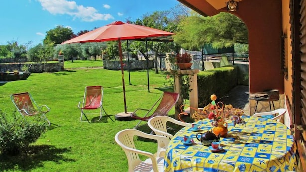 A patio with a table set for dining, surrounded by chairs, and a red umbrella providing shade. - Vacation home Milva by Interhome (Pula/Rakalj)