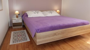 A bedroom with a wooden bed, purple bedding, two bedside lamps, a small bedside table, and a patterned rug. - Vacation home Milva by Interhome (Pula/Rakalj)