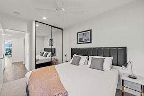 Une chambre moderne avec un grand lit, un ventilateur de plafond, une table de chevet avec une lampe et un tableau encadré au mur.